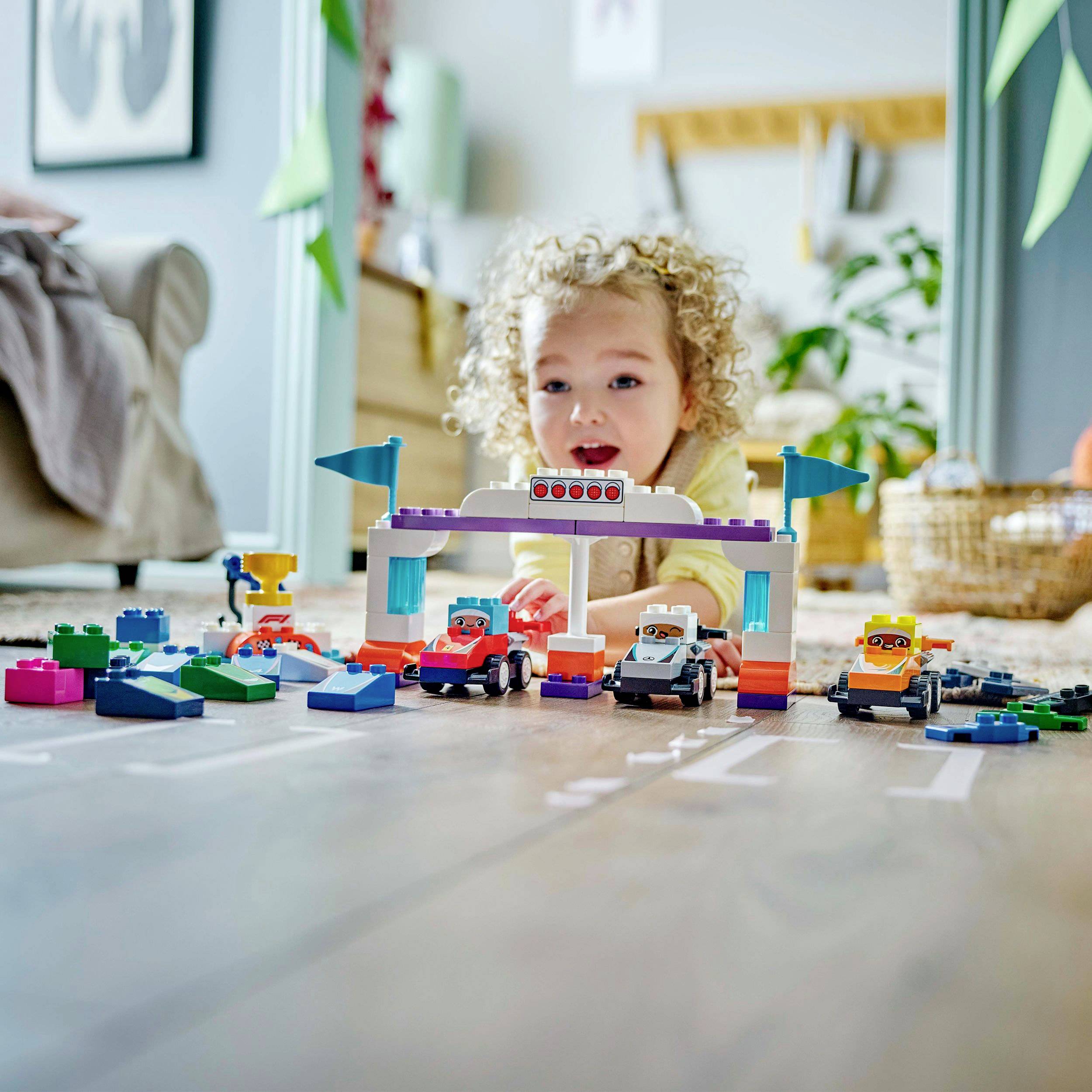 Ein Kleinkind spielt auf dem Boden mit bunten Bausteinen und Spielzeugautos in einem gemütlich eingerichteten Wohnzimmer.