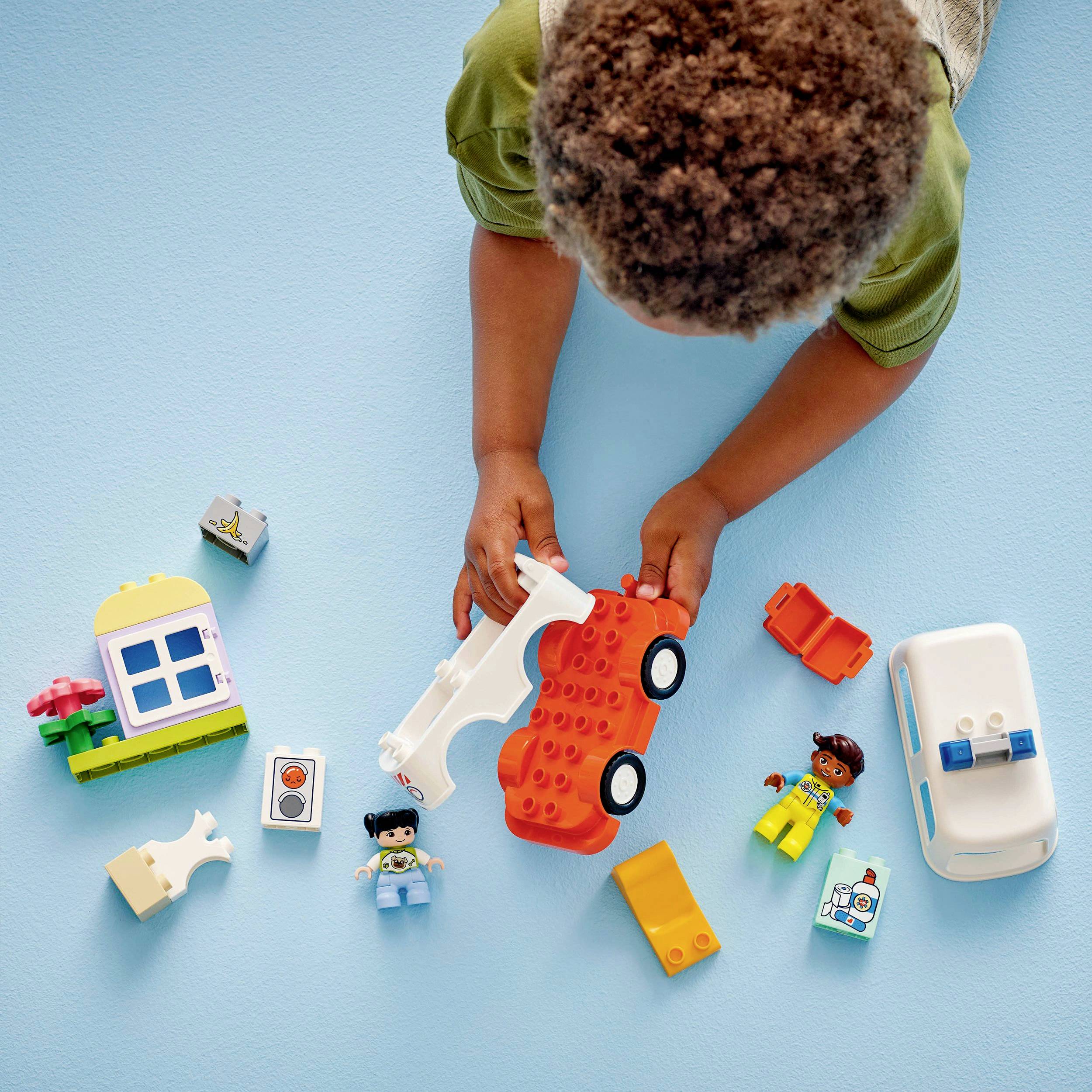 Ein Kleinkind spielt mit bunten Bauklötzen und Figuren auf einem blauen Hintergrund, darunter ein Auto und ein Haus.