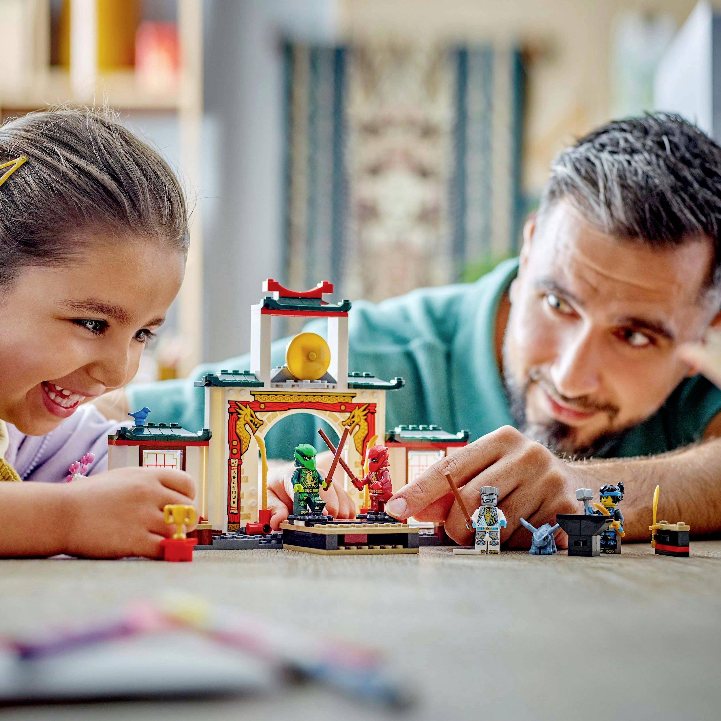 Ein Mann und ein Mädchen spielen lächelnd gemeinsam mit Bauklötzen auf einem Tisch, schaffen eine kleine Szene mit Figuren und Modellen.