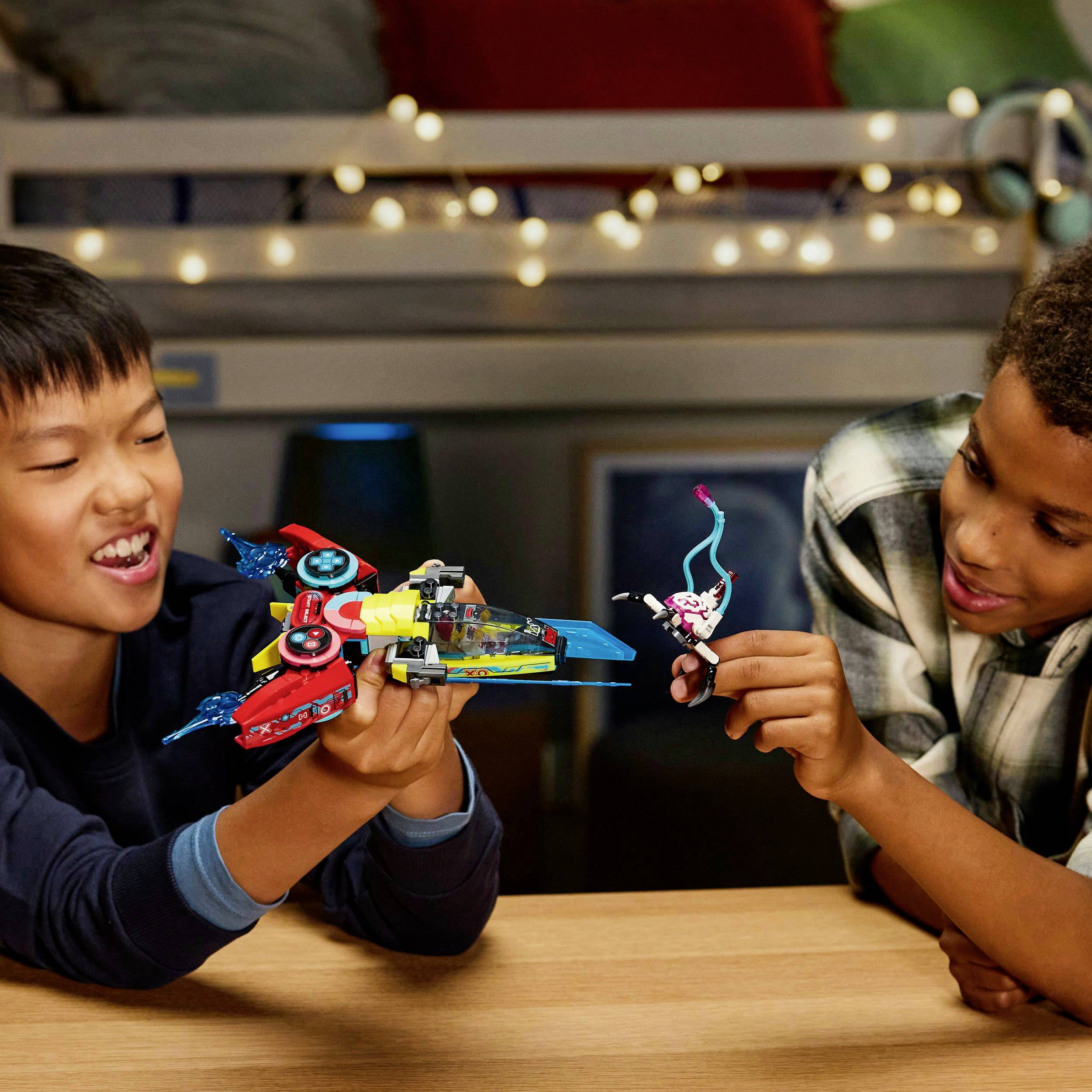 Zwei Jungen spielen gemeinsam mit Spielzeugrobotern auf einem Tisch. Sie lachen und wirken konzentriert. Im Hintergrund ist ein Etagenbett.