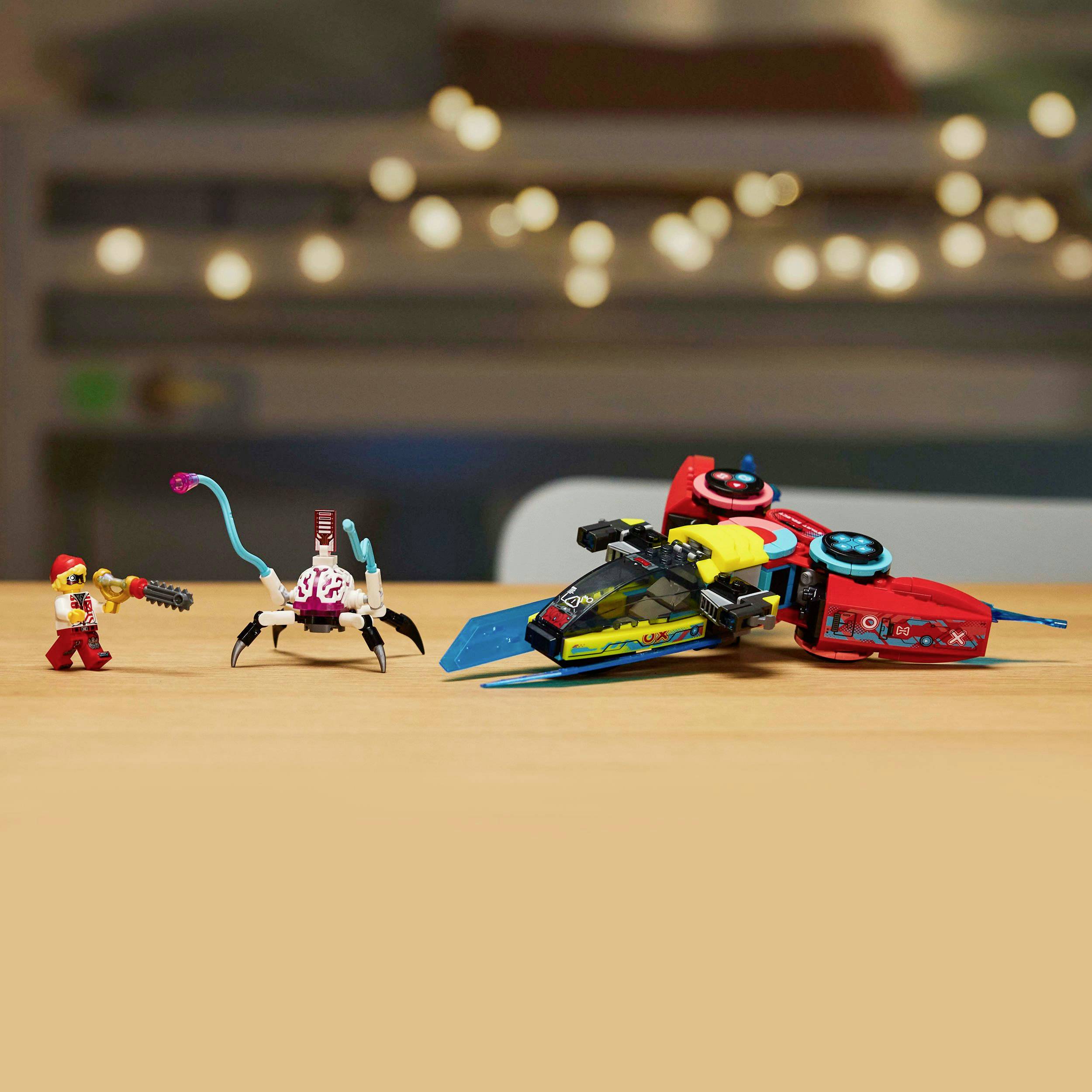 Ein bunter Spielzeugroboter und ein kleines Fahrzeug stehen auf einem Tisch. Im Hintergrund sind verschwommene Lichter zu sehen.