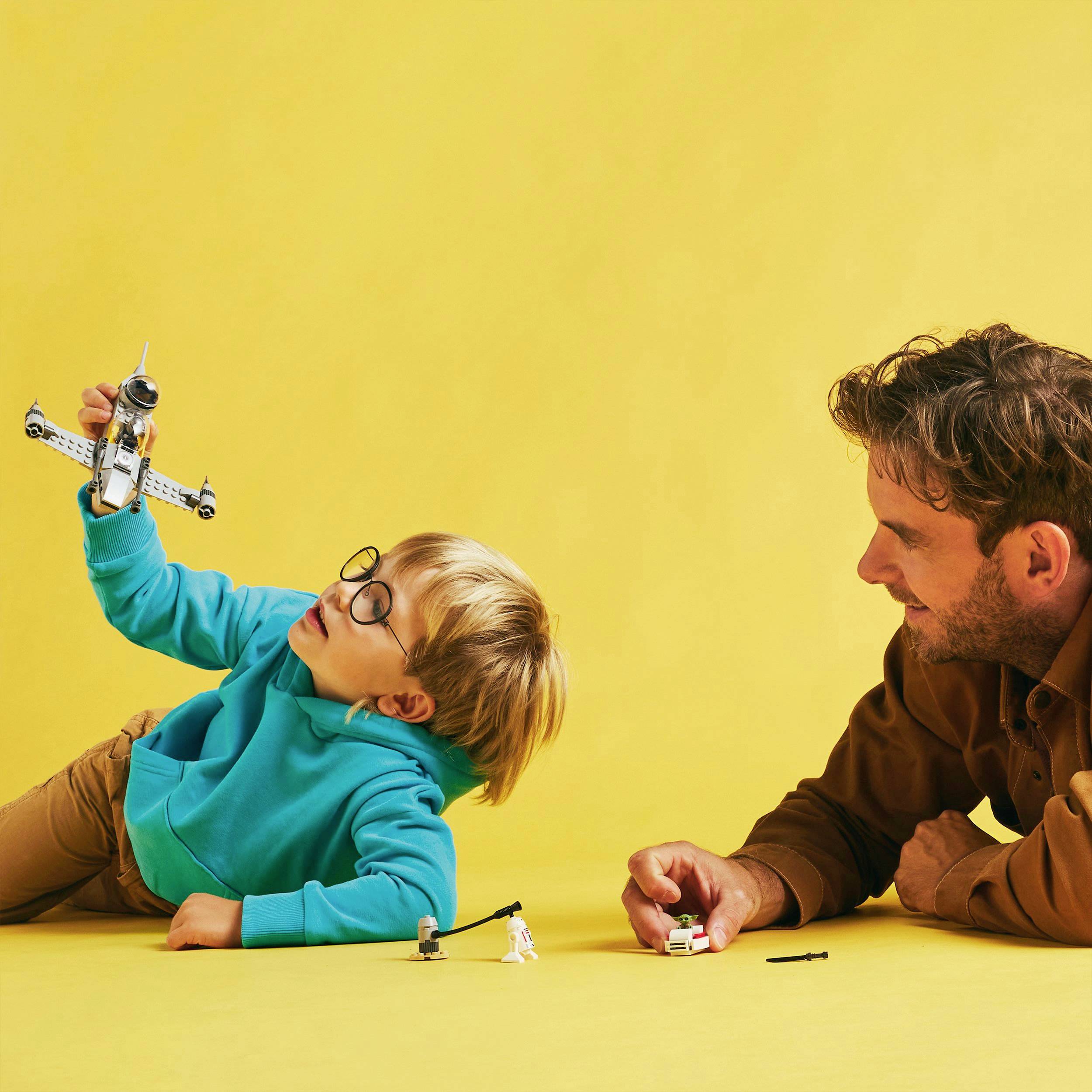 Ein Kind und ein Erwachsener spielen mit einem Spielzeugflugzeug und einer Spielfigur auf einem gelben Hintergrund.