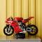 Ein rotes LEGO-Motorradmodell steht auf einem Tisch vor einem gelben Hintergrund. Das Modell zeigt detaillierte mechanische Teile.