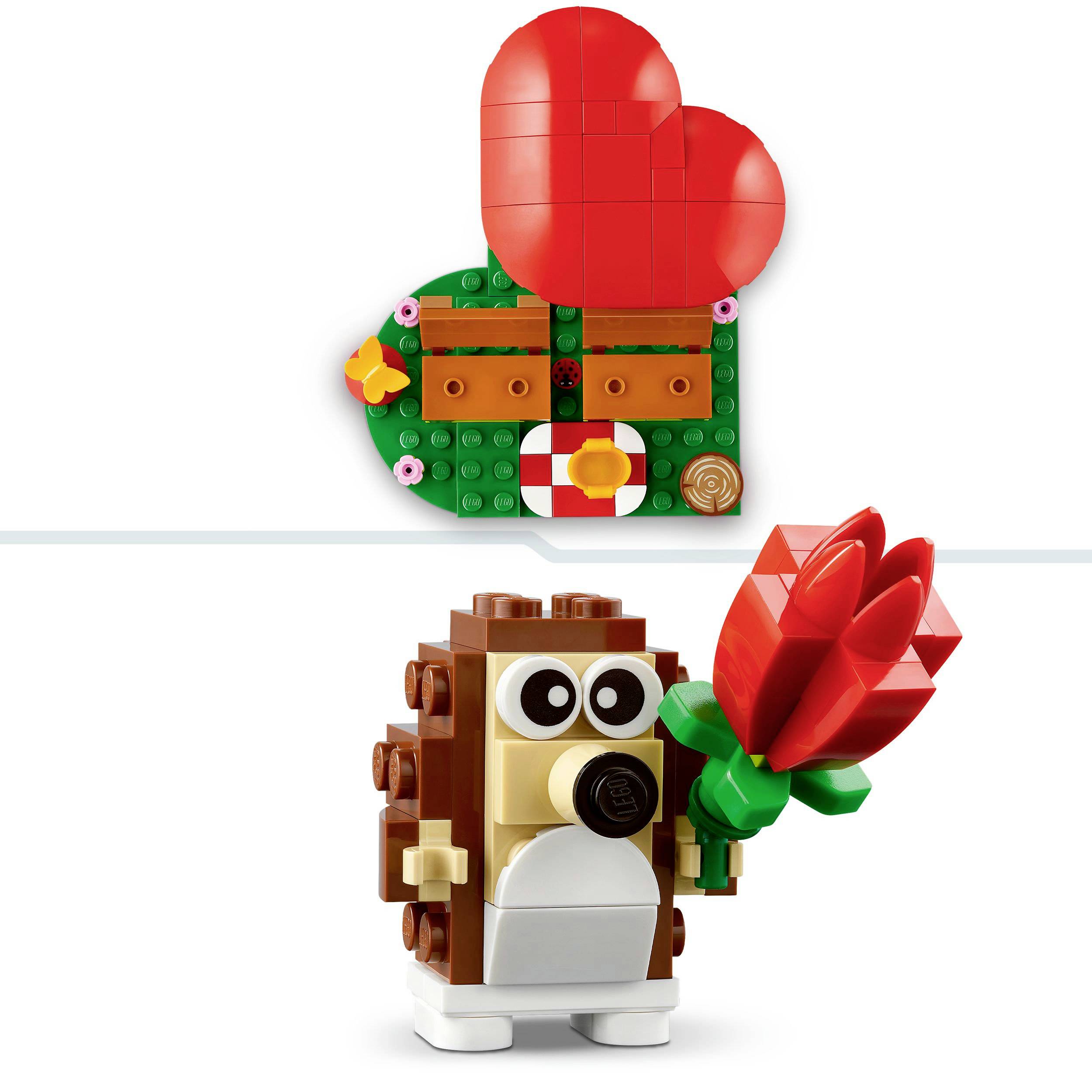 Ein Lego-Igel mit einer roten Blume steht vor einem herzförmigen, roten Lego-Element, das an eine Wand montiert ist.