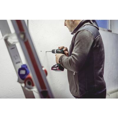 Mann bohrt mit einer elektrischen Bohrmaschine ein Loch in die weiße Wand. Eine Leiter steht im Vordergrund.