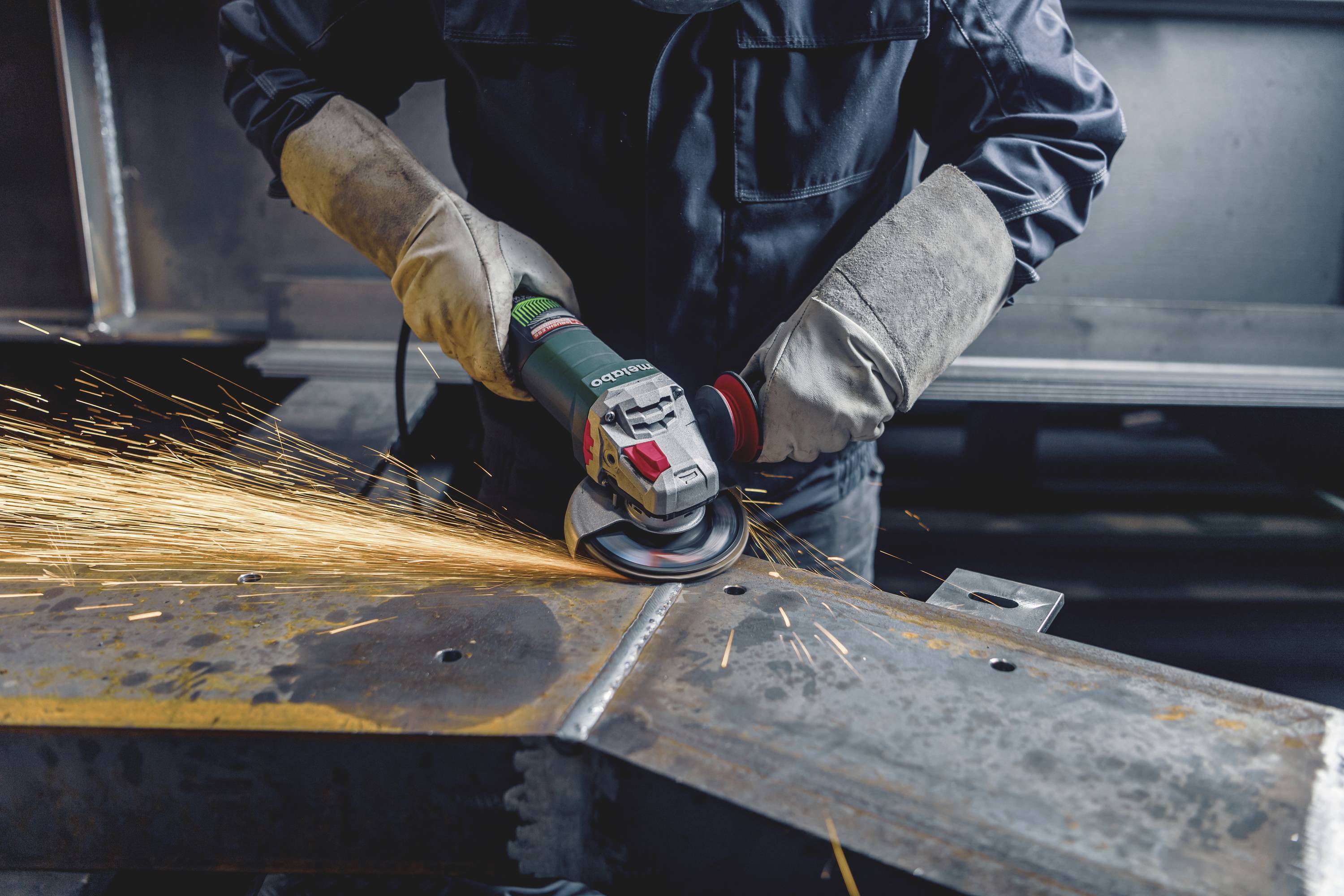 Arbeiter schleift Metallstück mit Funken sprühendem Schleifgerät in einer Werkstatt.