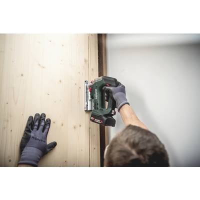 Eine Person benutzt einen Akkubohrer, um ein Holzbrett an eine Wand zu befestigen. Die Person trägt Arbeitshandschuhe.