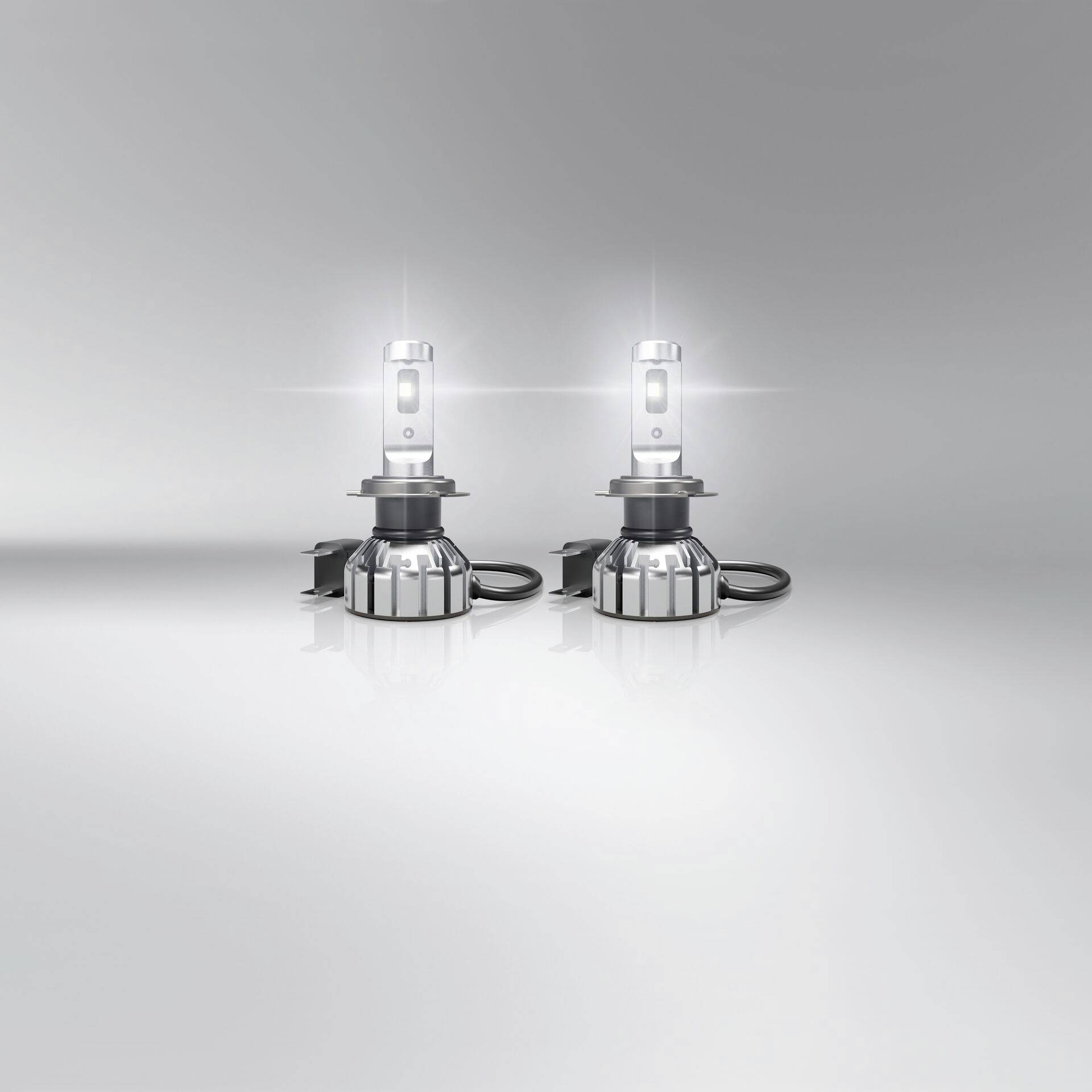 Zwei LED-Autoscheinwerfer leuchten auf einem reflektierenden Untergrund, strahlen helles, weißes Licht aus.