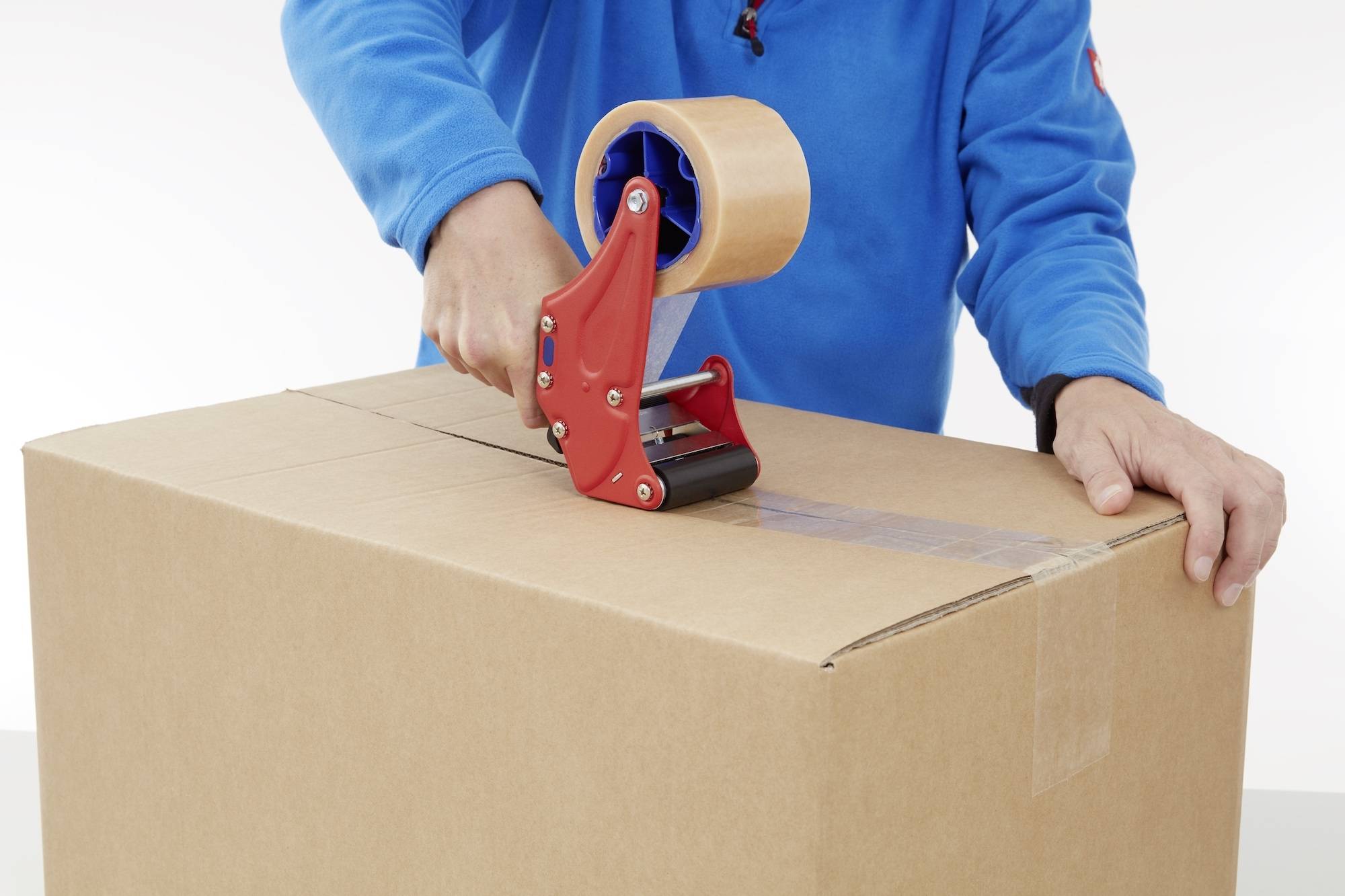 Person in blauem Shirt versiegelt einen großen Karton mit Klebeband.