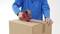 Person in blauem Pullover versiegelt einen Karton mit Klebeband.
