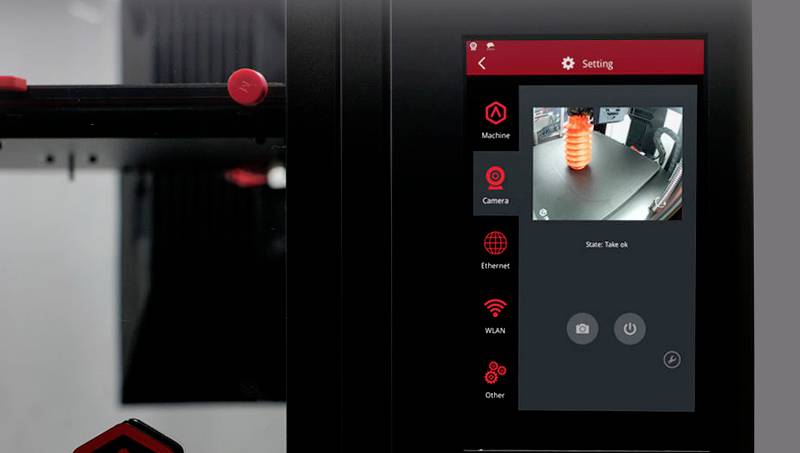 3D-Drucker-Bedienfeld mit Kamera-Feed zeigt fortschreitenden Druck eines spiralförmigen, orangefarbenen Objekts auf dem Druckbett.