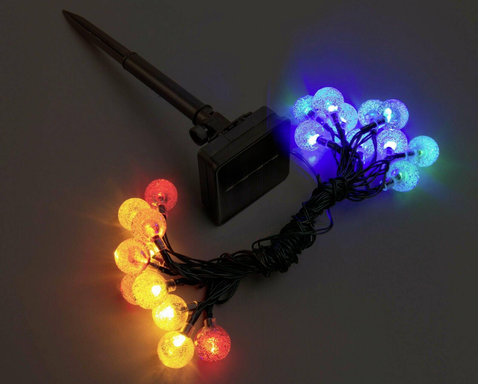 Bunte LED-Lichterkette mit runden Glühbirnen, angeschlossen an ein Solarpanel auf einem dunklen Hintergrund.