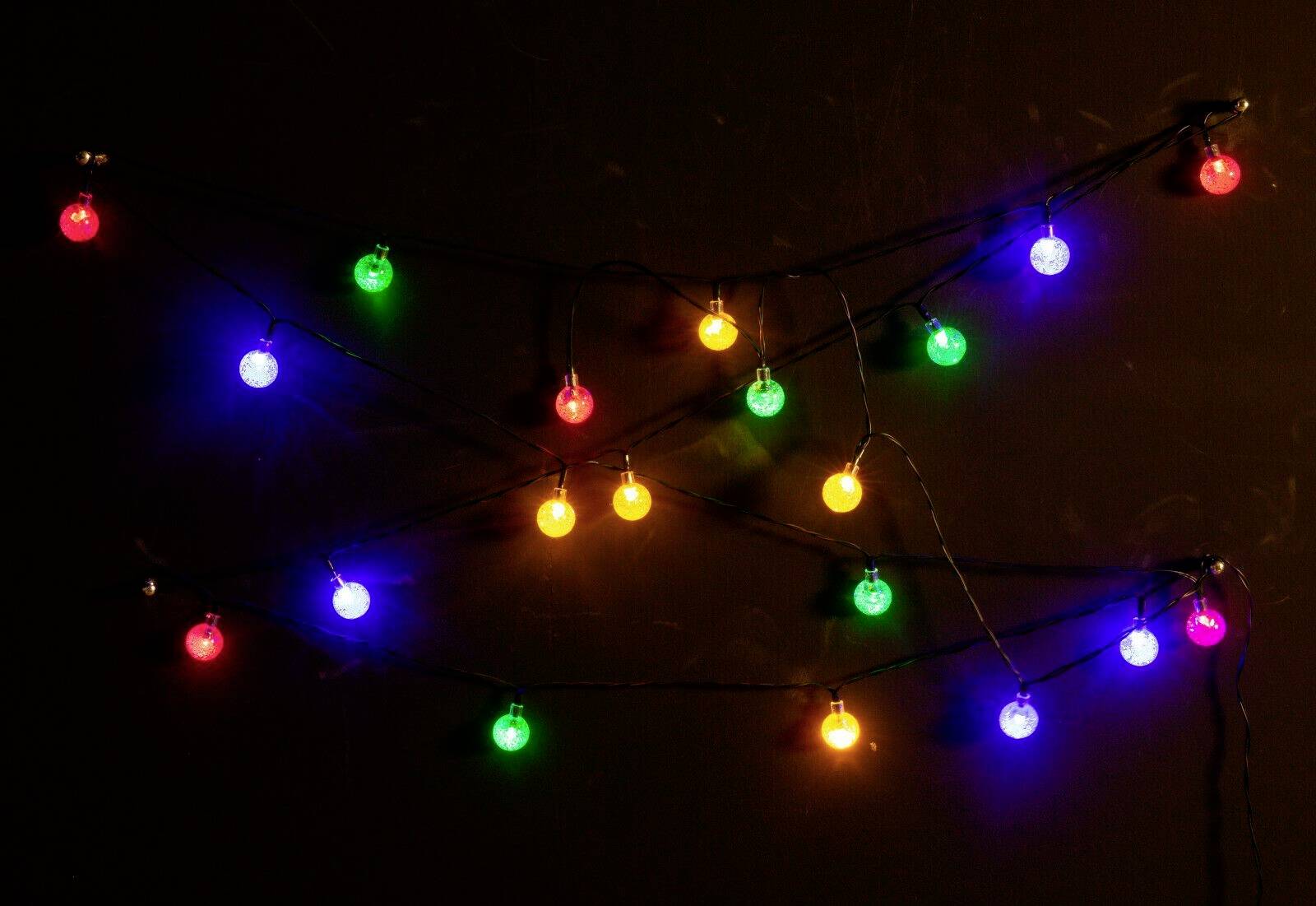 Bunte Lichterketten mit roten, blauen, grünen und gelben Lichtern, die in zwei Reihen an einer dunklen Wand hängen.
