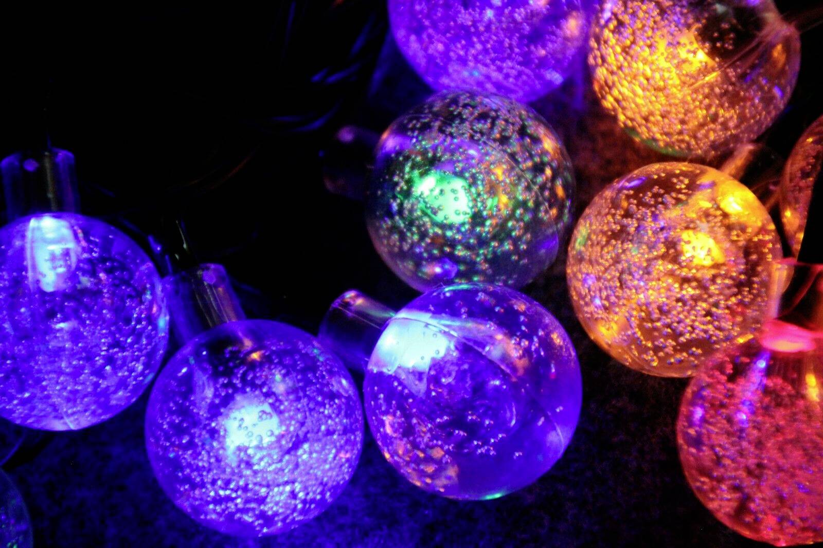 Bunte Lichterkettenkugeln leuchten in Blau, Lila, Grün und Orange auf dunklem Hintergrund. Sie erzeugen eine festliche Atmosphäre.
