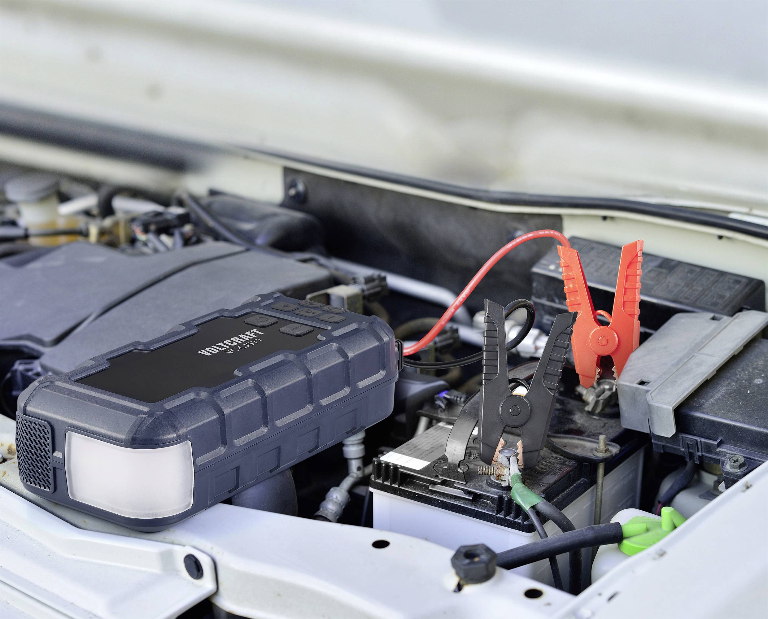 Ein Starthilfegerät ist an eine Autobatterie angeschlossen, um Strom zu liefern. Rotes und schwarzes Kabel sind an den Batteriepolen befestigt.