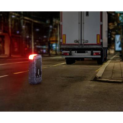 Ein kleiner, leuchtender Koffer steht nachts auf der Straße vor einem geparkten Lastwagen. Die Szene ist städtisch und beleuchtet.