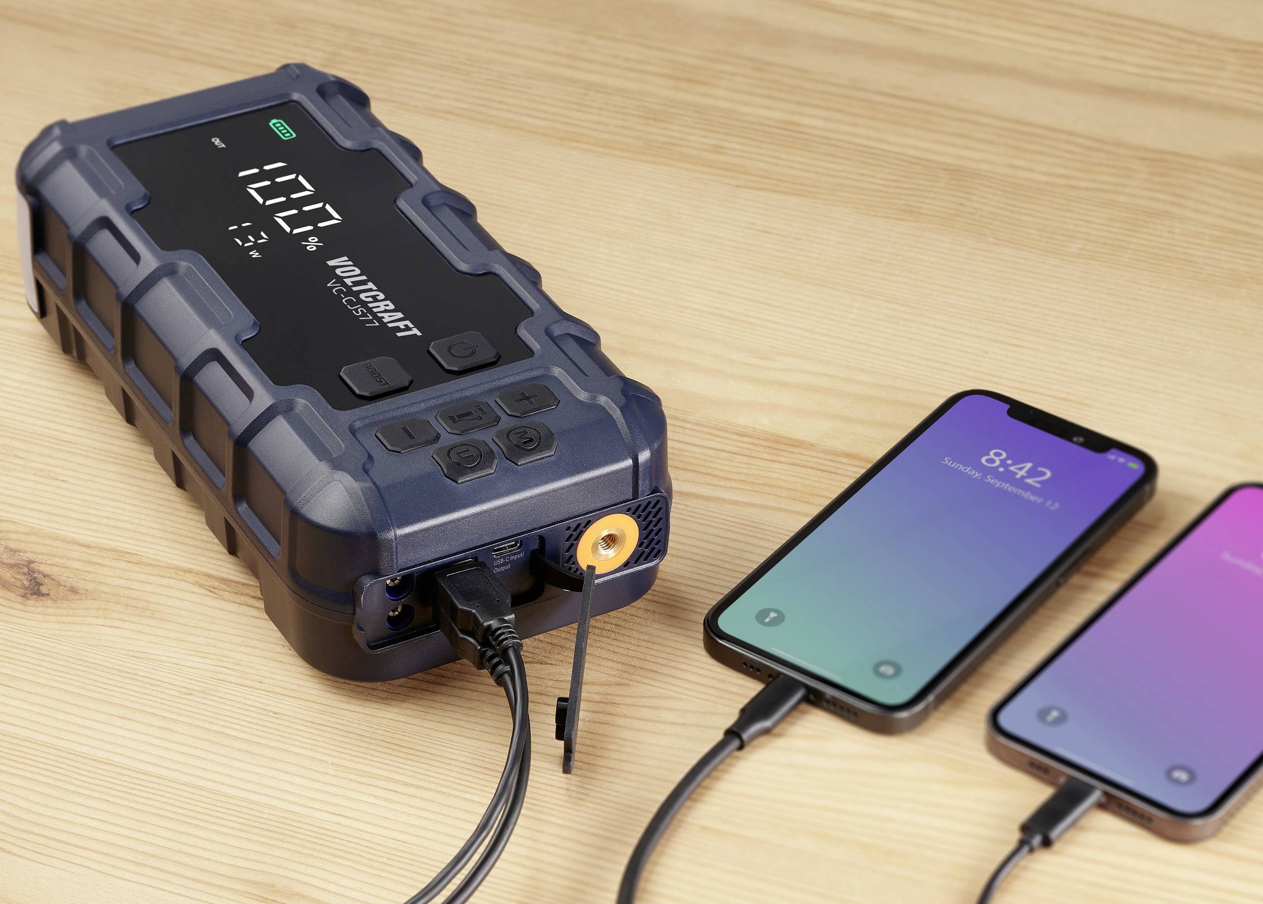 Ein tragbares Ladegerät lädt zwei Smartphones auf. Das Display zeigt '100%' an, was den vollen Ladezustand des Geräts anzeigt.