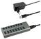 USB-Hub mit sieben Ports, fünf schwarz, zwei blau markiert, verbunden mit einem Netzkabel und einem USB-Kabel für Stromversorgung und Datenübertragung.
