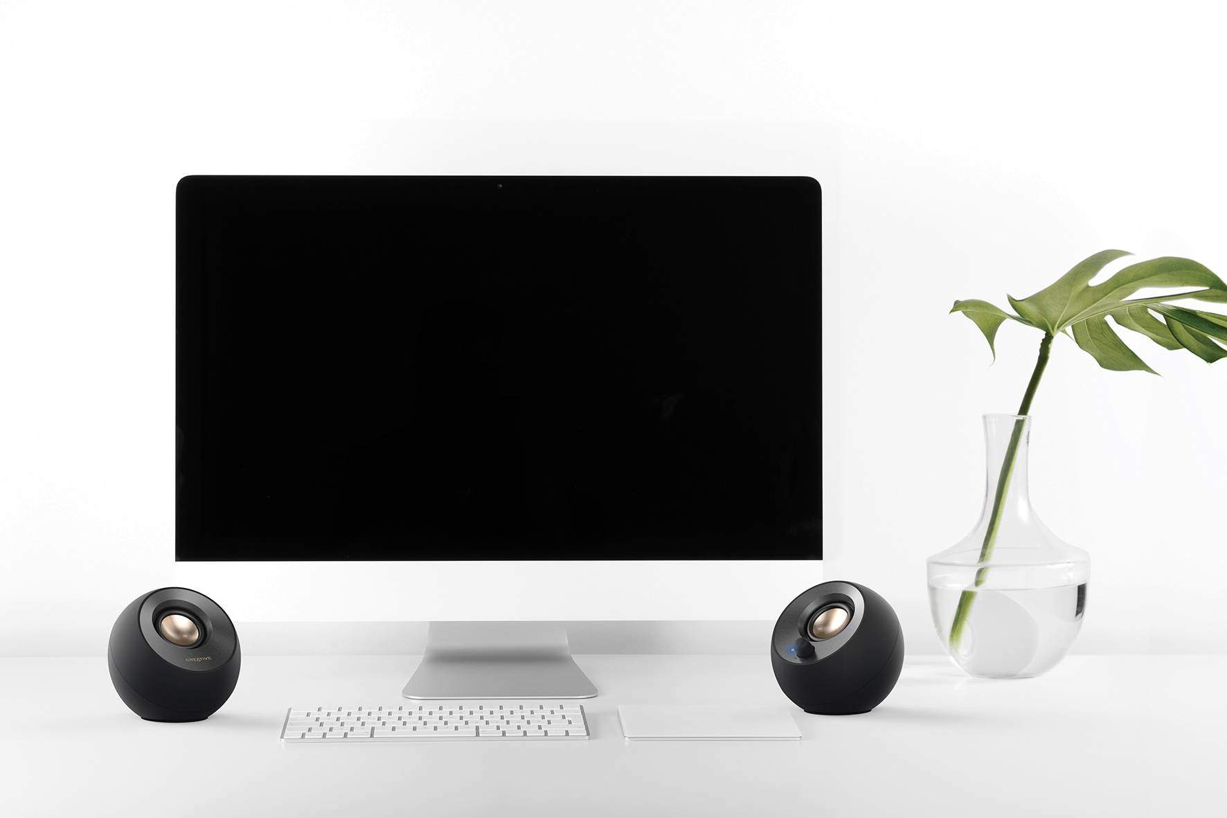 'Moderner Schreibtisch mit iMac, zwei Lautsprechern und Vase mit grünem Blatt auf weißem Hintergrund.'