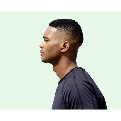 Eine Person mit kurzen Haaren und Ohrstöpseln schaut zur Seite, vor einem hellgrünen Hintergrund. Sie trägt ein schwarzes Shirt.