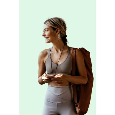 Eine lächelnde Person in Sportkleidung hält ein Handy und eine Sporttasche über der Schulter, vor einem hellgrünen Hintergrund.
