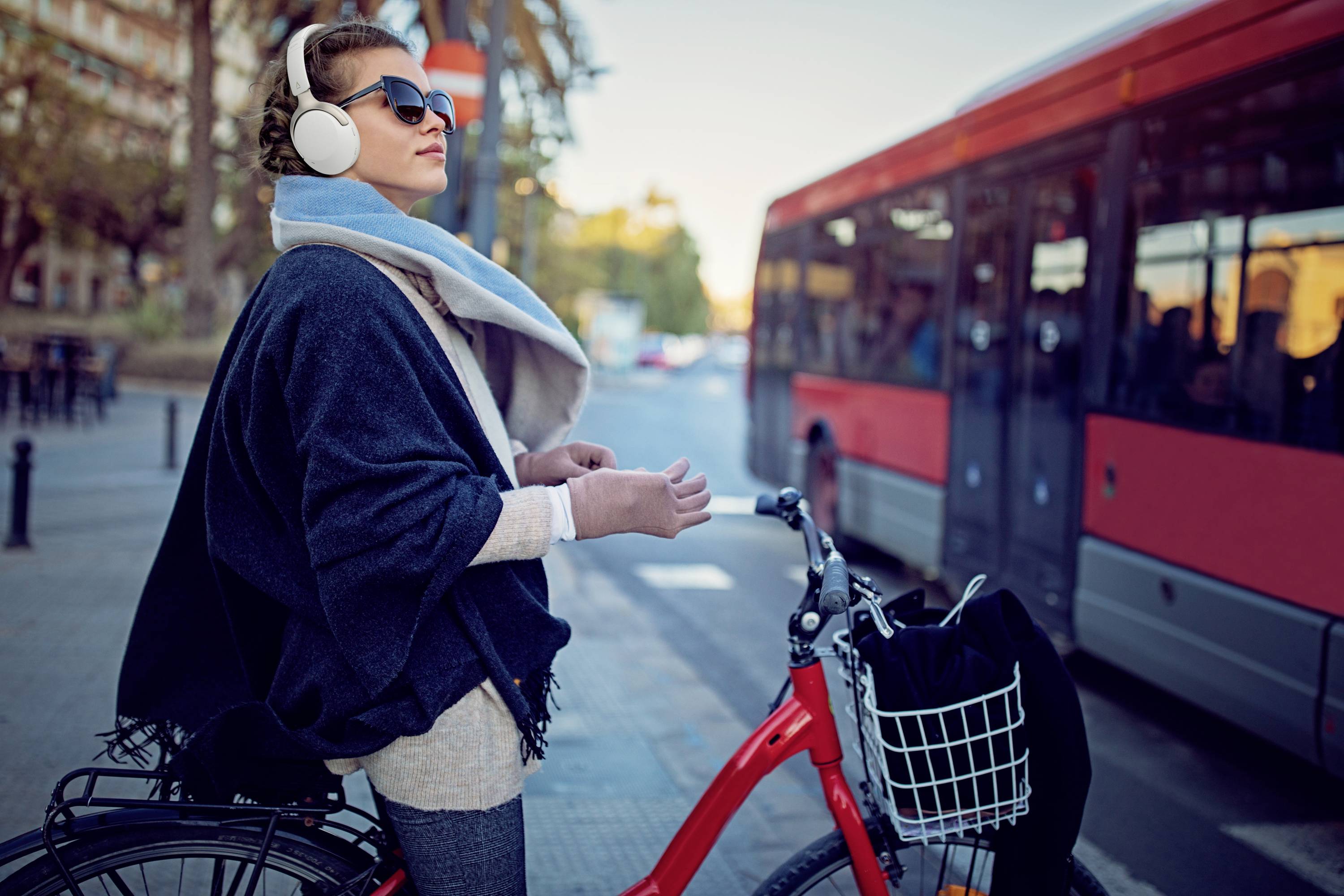 Frau mit Kopfhörern auf blauem Fahrrad, wartet an einer Kreuzung neben einem roten Bus.