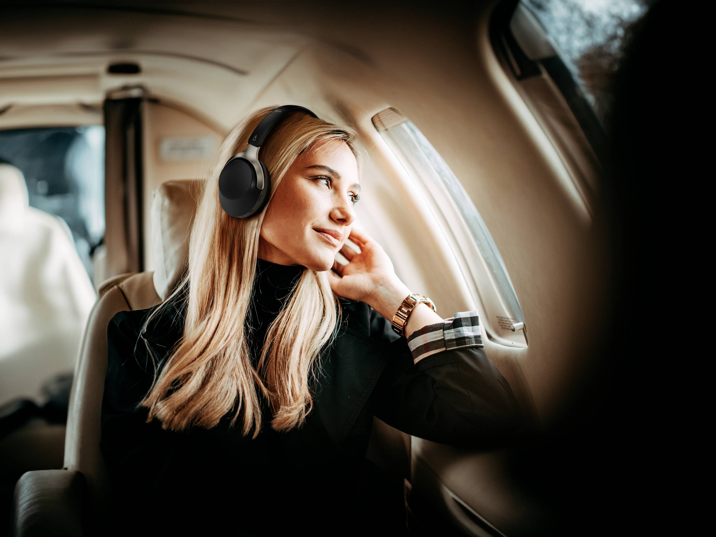 Eine Frau mit Kopfhörern schaut aus dem Fenster eines Flugzeugs. Sie scheint entspannt zu sein und genießt die Aussicht.