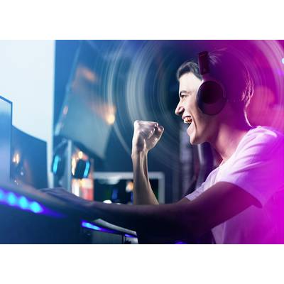 Ein junger Mensch mit Kopfhörern feiert freudig am Computer. Die Szene ist bunt beleuchtet, was auf ein dynamisches Spielerlebnis hindeutet.