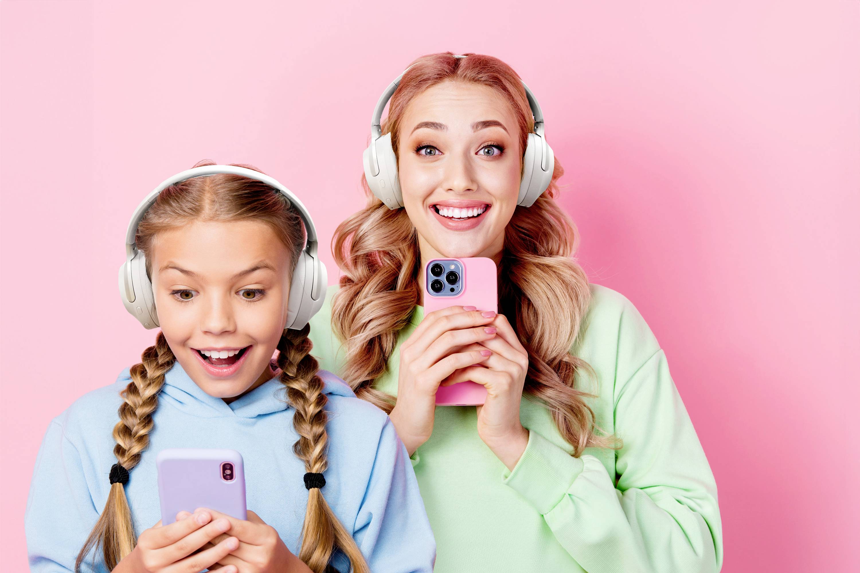 Zwei fröhliche Personen mit Kopfhörern halten Smartphones vor einem rosa Hintergrund. Sie scheinen sich über etwas auf den Bildschirmen zu freuen.