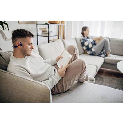 Ein Mann und eine Frau sitzen auf einem Sofa in einem Wohnzimmer und lesen jeweils ein Buch. Der Mann trägt kabellose Kopfhörer.