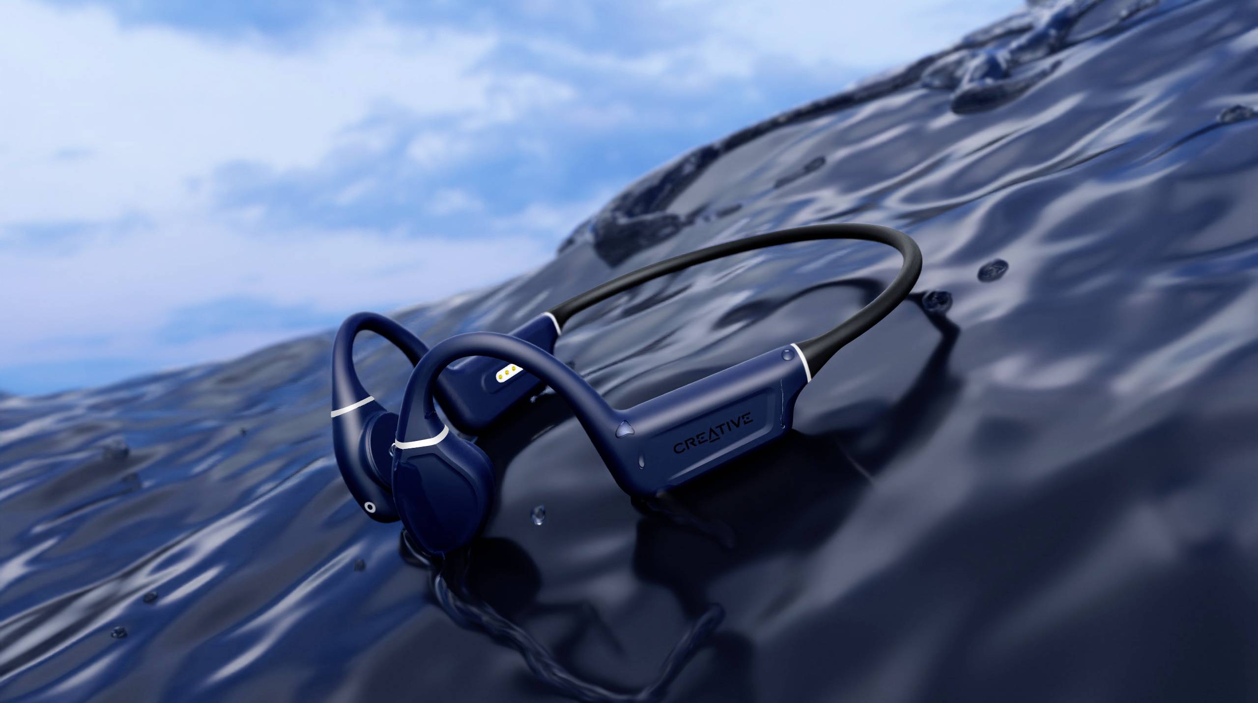 Dunkelblauer Kopfhörer schwimmt auf glänzender Wasseroberfläche, blauer Himmel im Hintergrund.