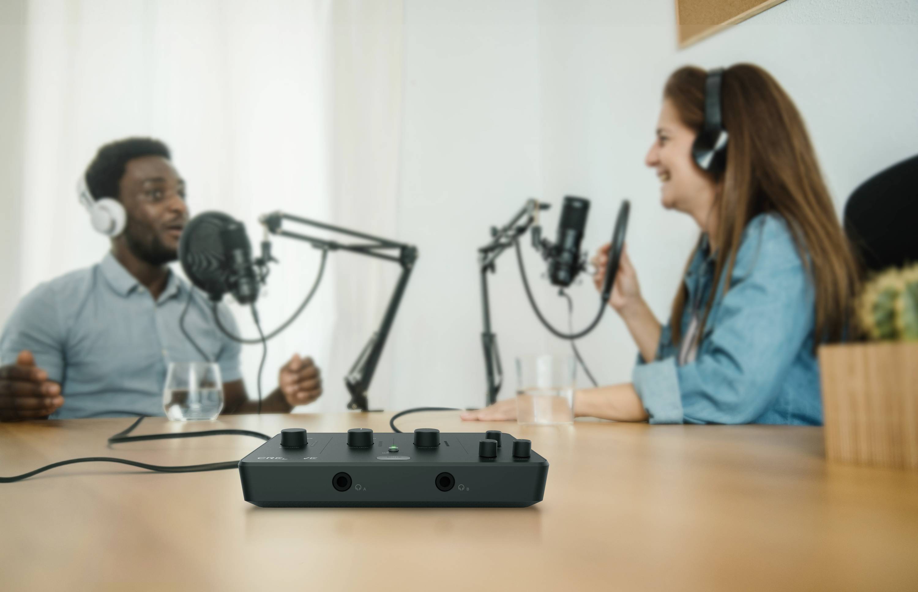 Zwei Personen unterhalten sich in einem Aufnahme-Podcaststudio mit Mikrofonen und Audiomischpult auf einem Holztisch.