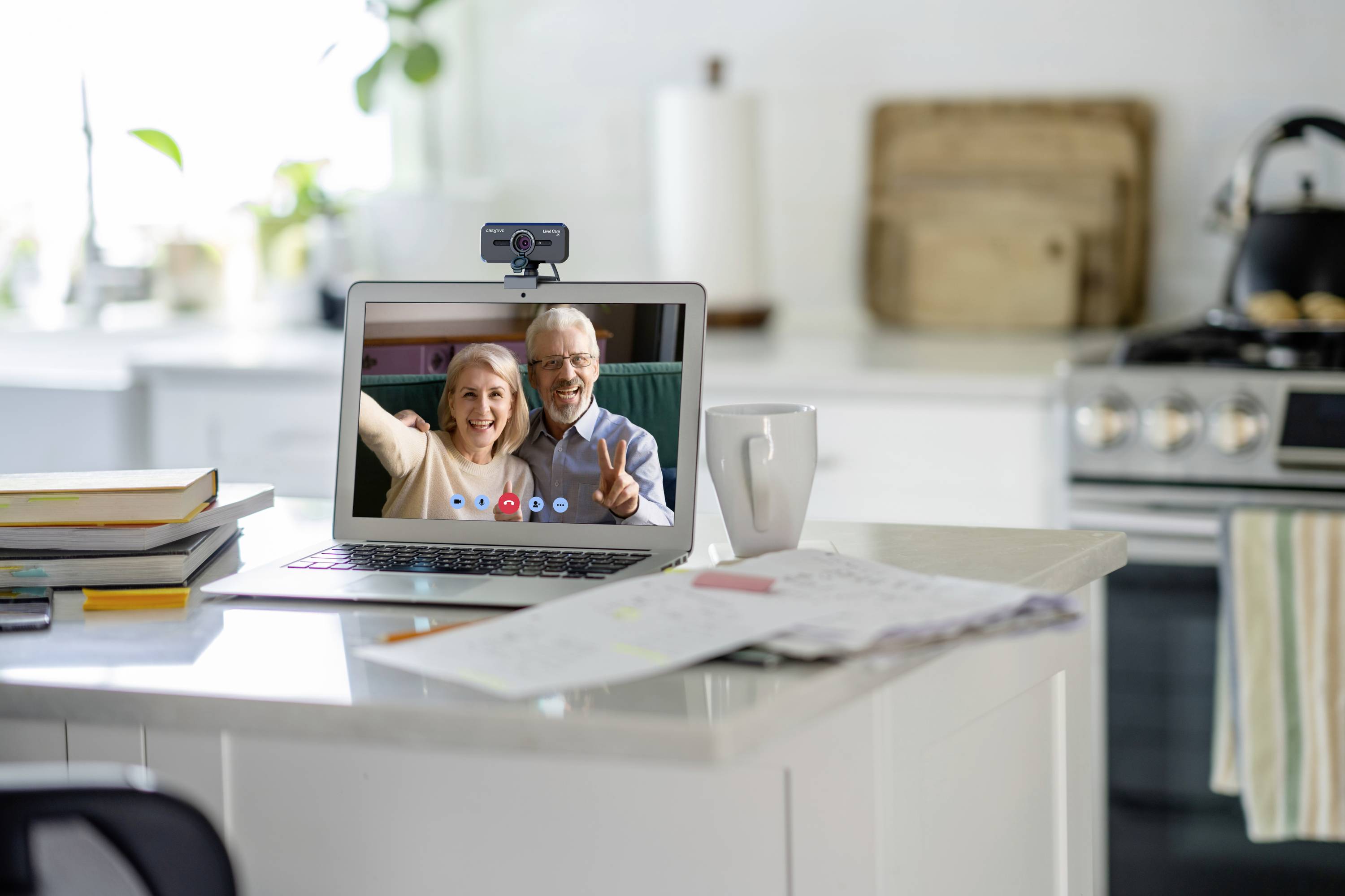 Ein Laptop auf einem Küchentresen zeigt ein Videotelefonat mit zwei fröhlich winkenden älteren Personen auf dem Bildschirm.