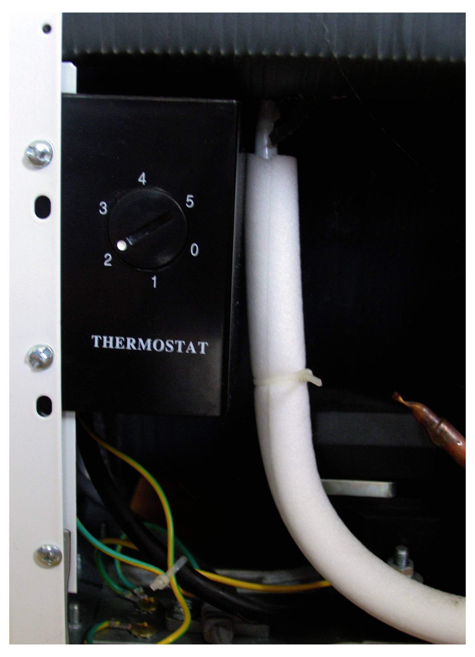 Thermostat-Einstellung in einem elektrischen Gerät, Skala von 1 bis 5, umgeben von Kabeln und Rohren.