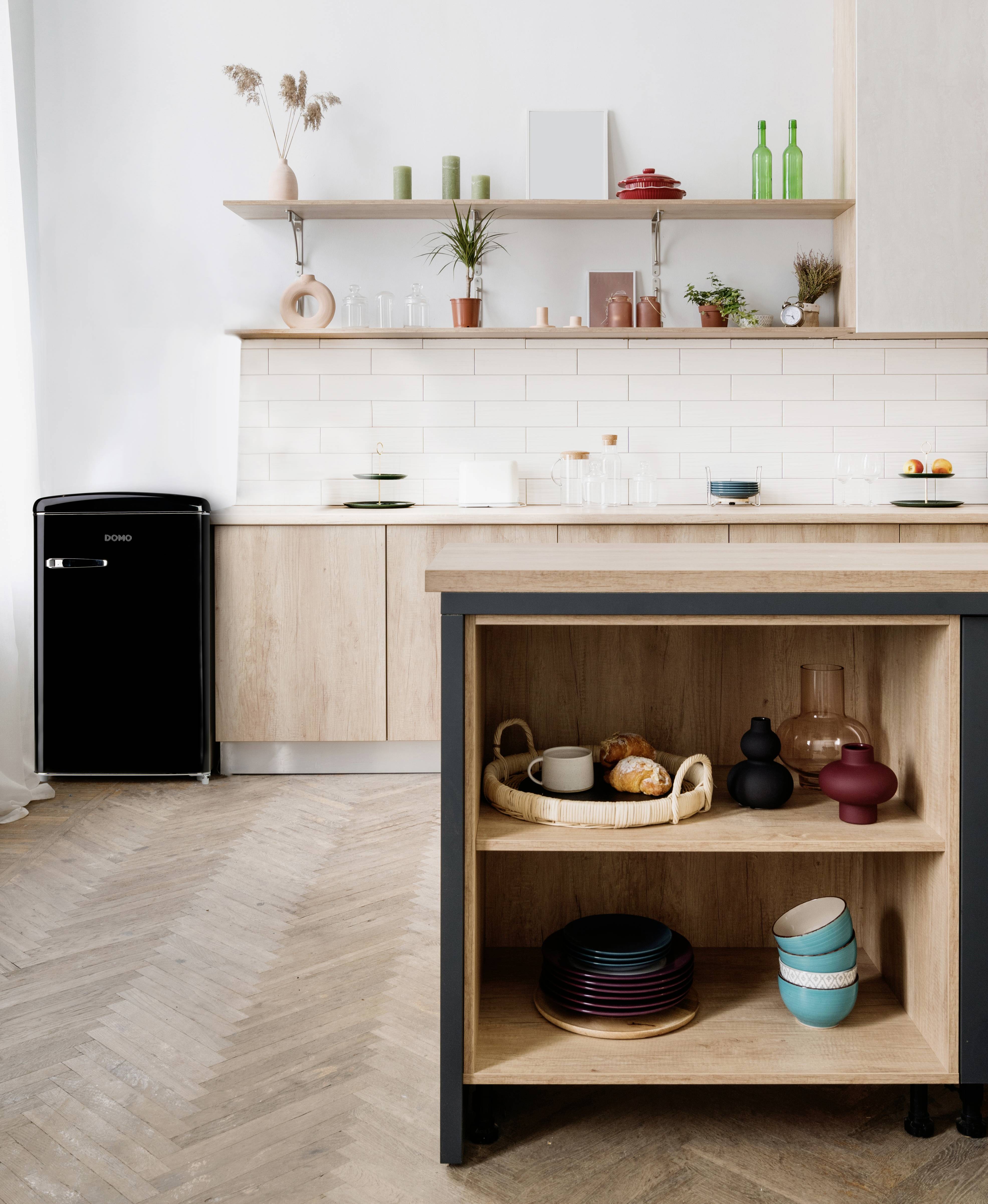 Helle, moderne Küche mit Holzregalen, einem schwarzen Kühlschrank und pastellfarbenem Geschirr auf einer Arbeitsplatte und im Regal.