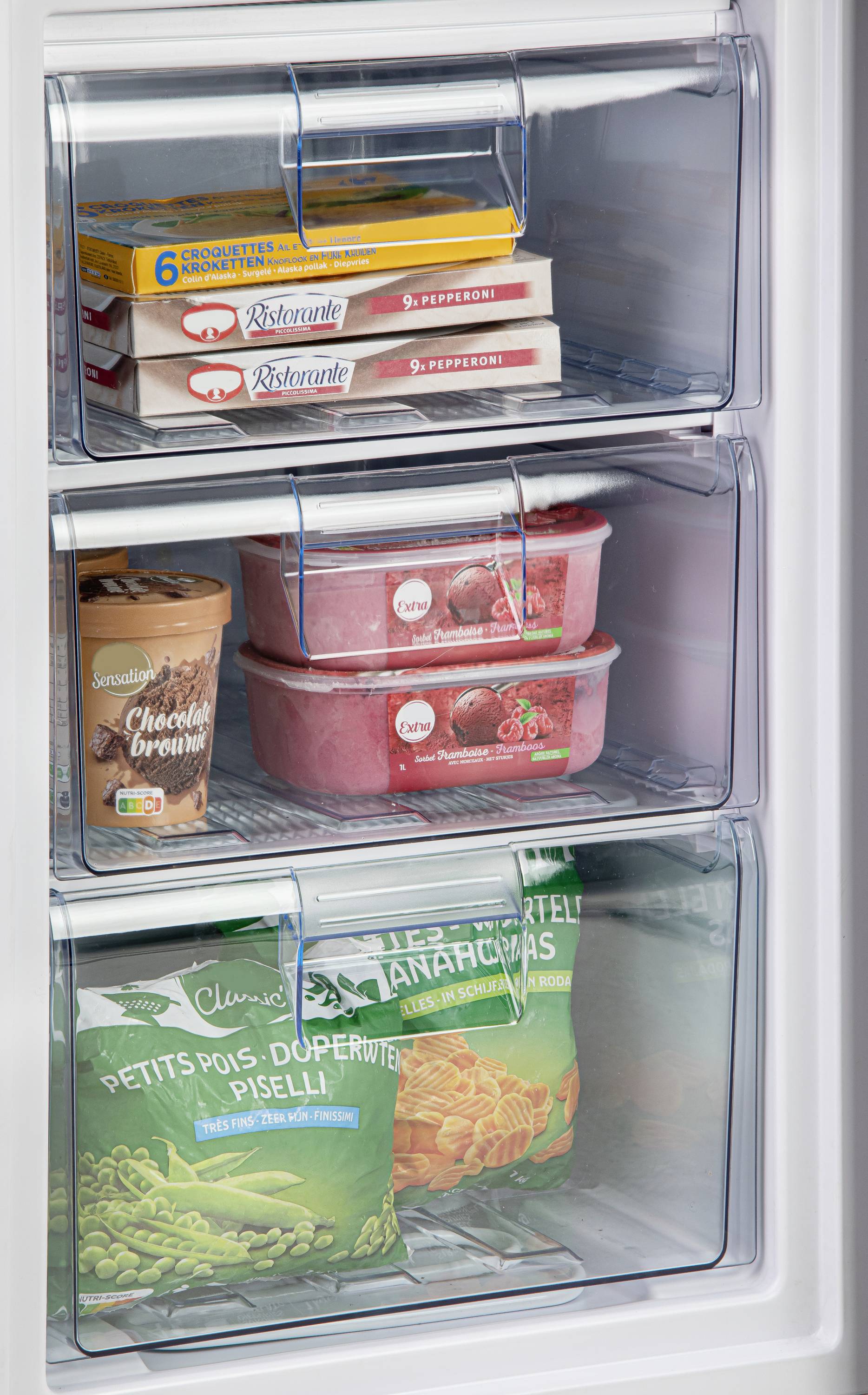 Eine offene Gefrierschranktür zeigt drei Fächer mit Tiefkühlprodukten: Pizza, Eis, Tiefkühlgemüse. Sichtbare Marken auf den Verpackungen.