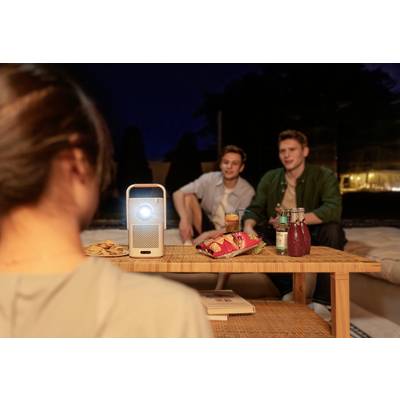 Ein Beamer projiziert ein Bild in einer nächtlichen Outdoor-Szene. Zwei Personen sitzen, Getränke und Snacks stehen auf einem Tisch.