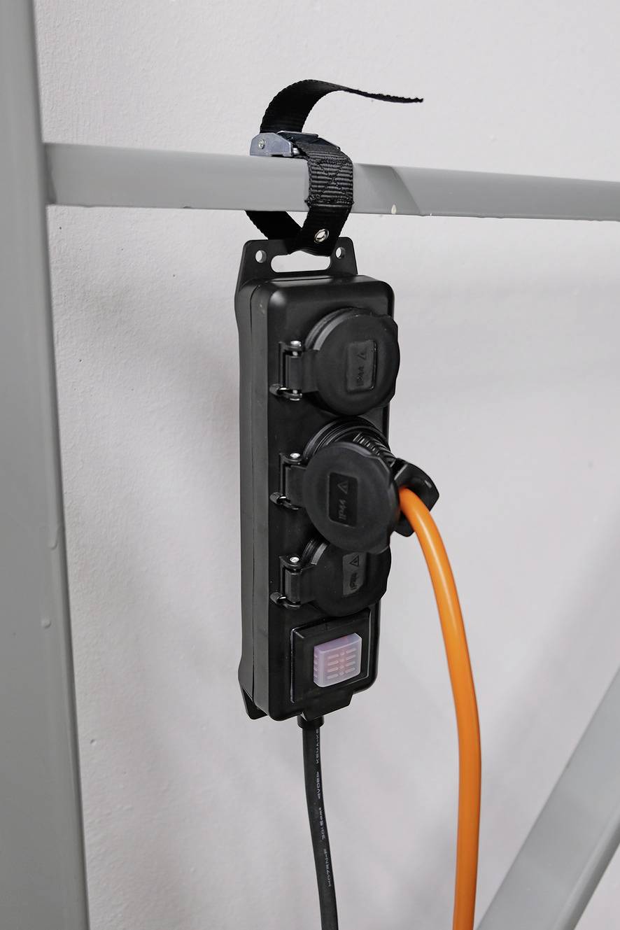 Ein Mehrfachstecker mit drei Steckdosen ist an einer Metallstange befestigt. Ein orangefarbenes Kabel ist eingesteckt.