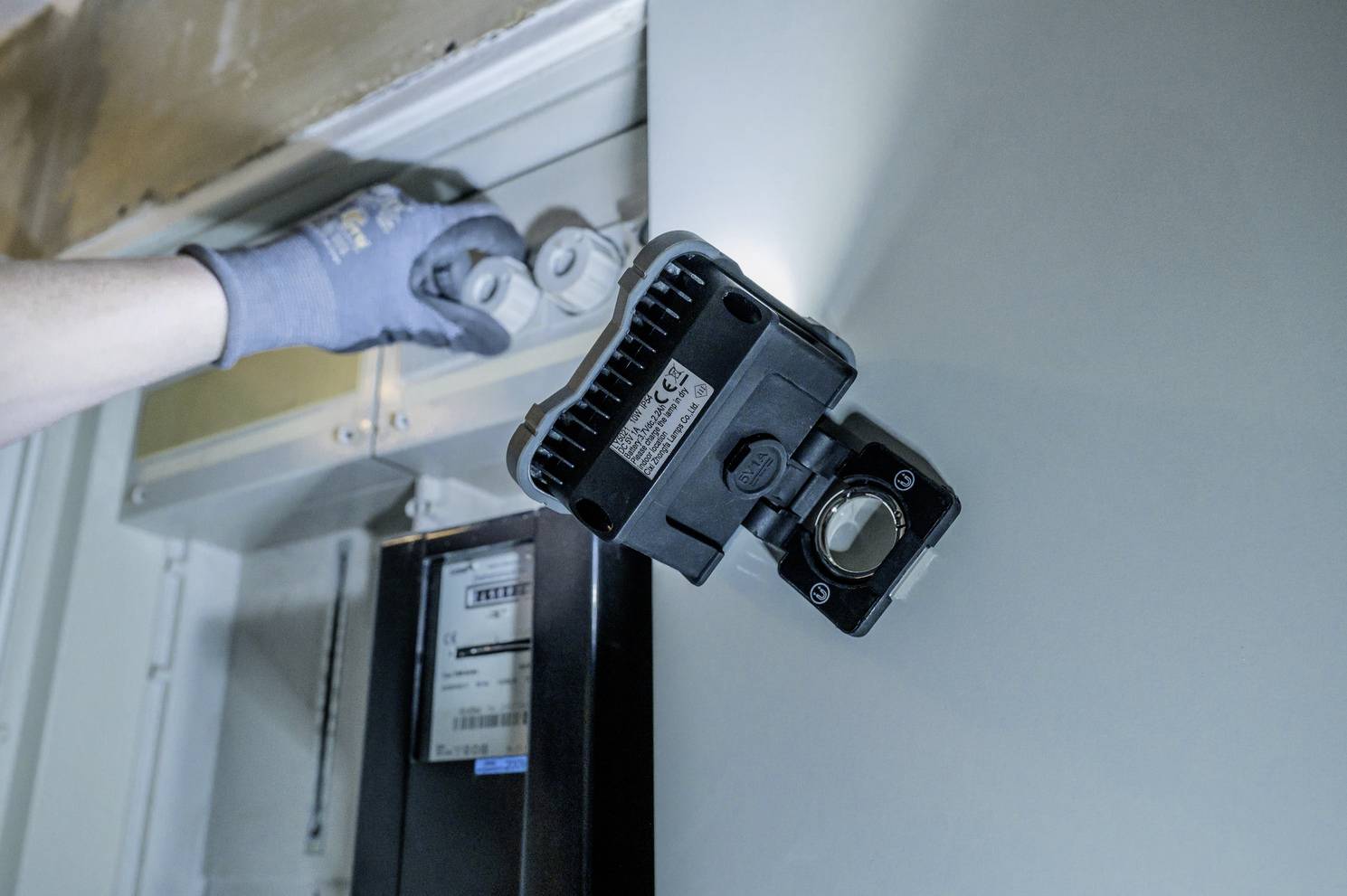 Eine Person mit Handschuhen installiert oder wartet eine mechanische Komponente, möglicherweise einen Zähler oder eine Messvorrichtung, an einer Wand.