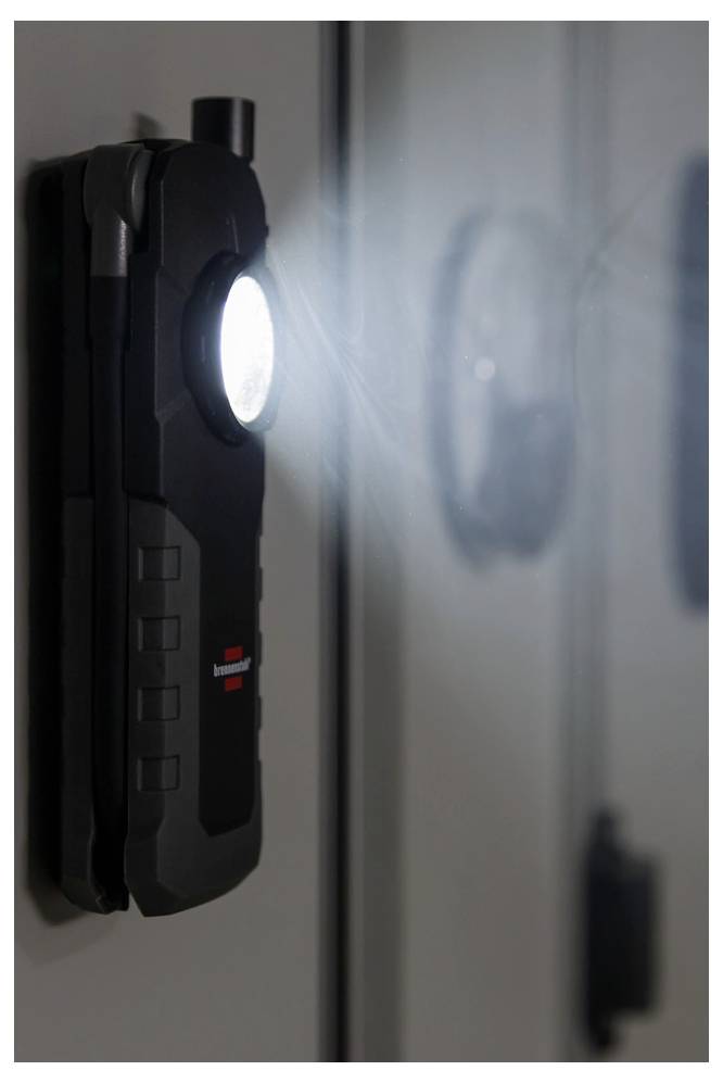 Eine an der Wand montierte schwarze Ladestation oder ein Gerät mit einem hellen kreisförmigen Licht, in Nahaufnahme neben einer reflektierenden Oberfläche betrachtet.