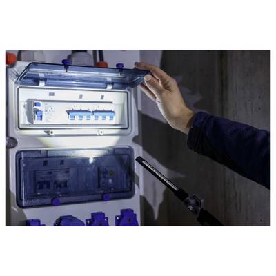 Person inspecting ein offenes Elektroverteilerpanel mit leuchtenden Schutzschaltern, während sie die Tür hält, was auf Wartungs- oder Installationsarbeiten hindeutet.