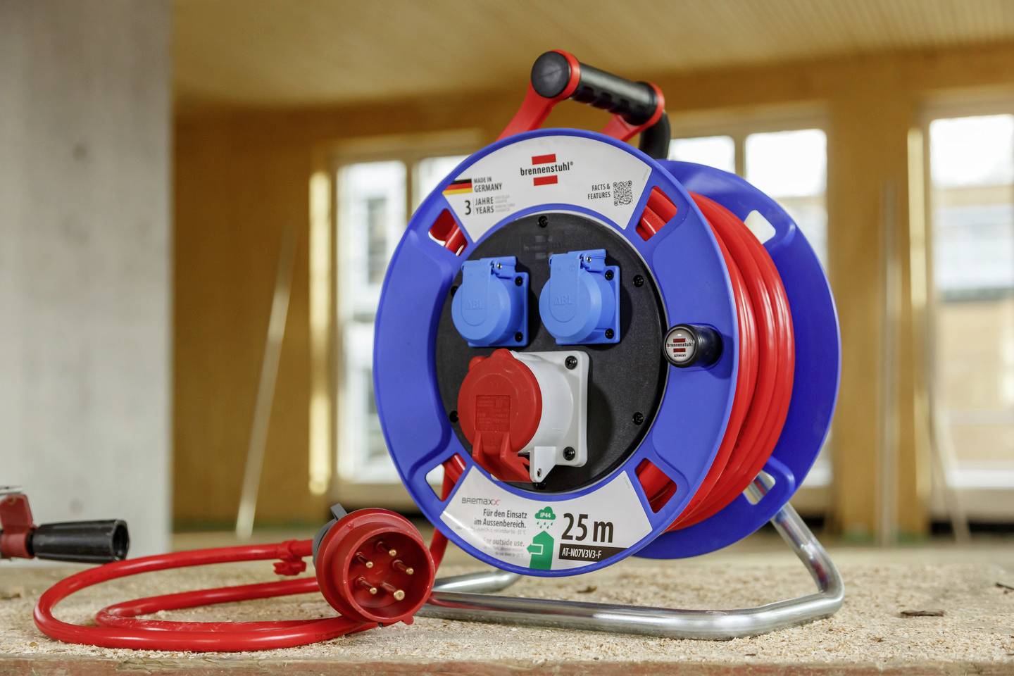 Eine Kabeltrommel mit 25 m rotem Kabel und Steckdosen, platziert in einer Baustellenumgebung.