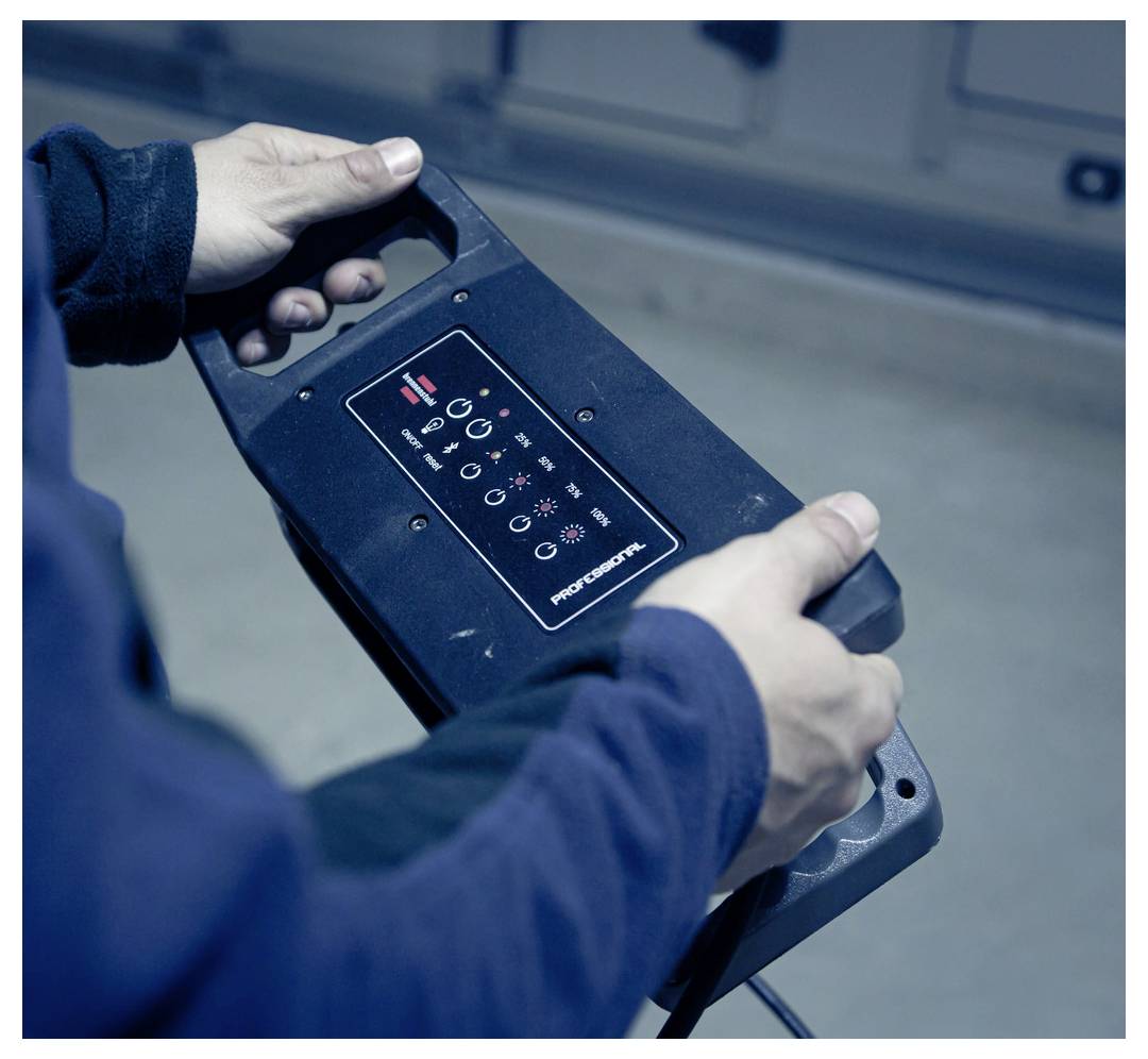 Person holding a black power tool or battery pack with a control panel and icons, shown close-up indoors.<br><br>Person mit schwarzem Elektrowerkzeug oder Akku mit Bedienfeld und Symbolen, nahaufnahme in Innenräumen gezeigt.