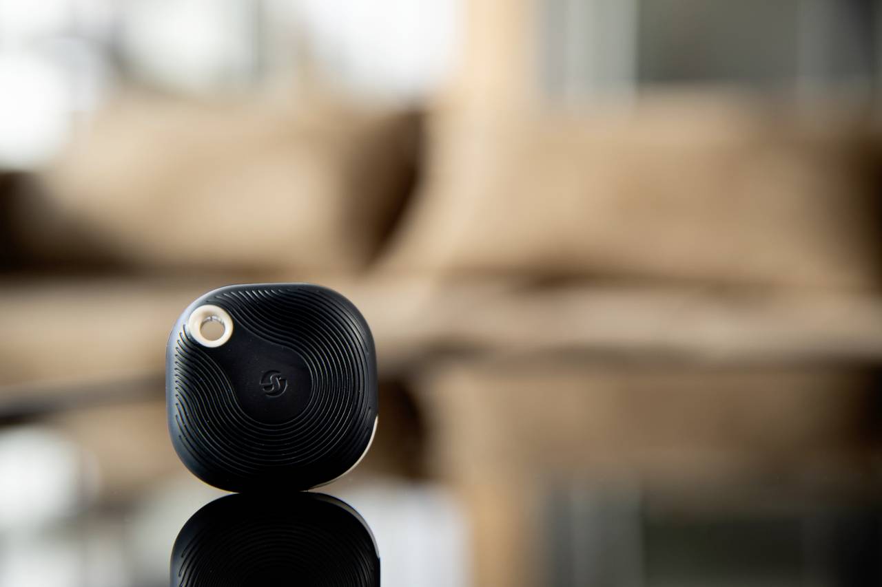 Ein kleiner, schwarzer, quadratischer Bluetooth-Tracker liegt auf einer glänzenden Oberfläche, unscharfer Hintergrund.