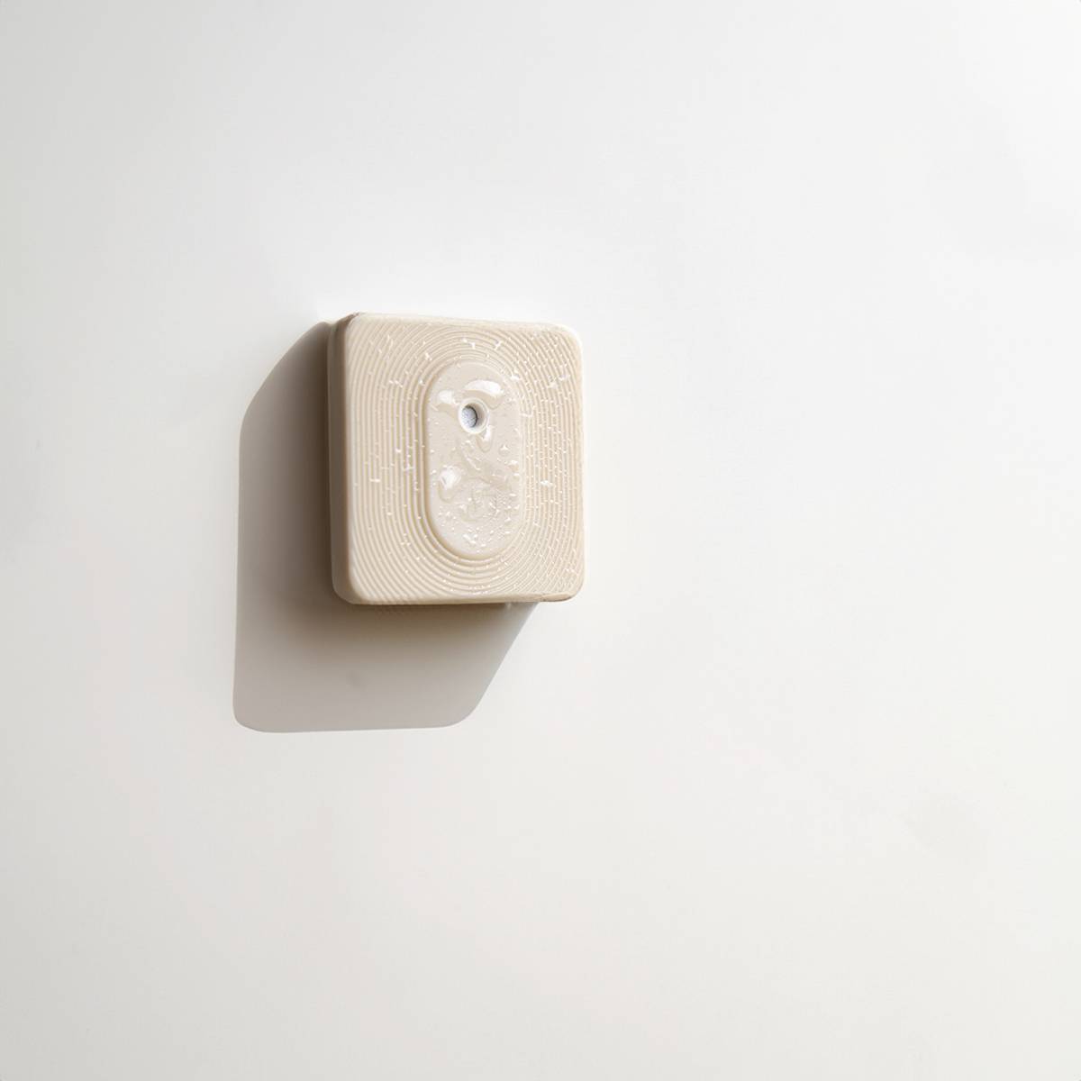 Ein weißer Lichtschalter im minimalistischen Design an einer weißen Wand. Die Beleuchtung wirft einen sanften Schatten.