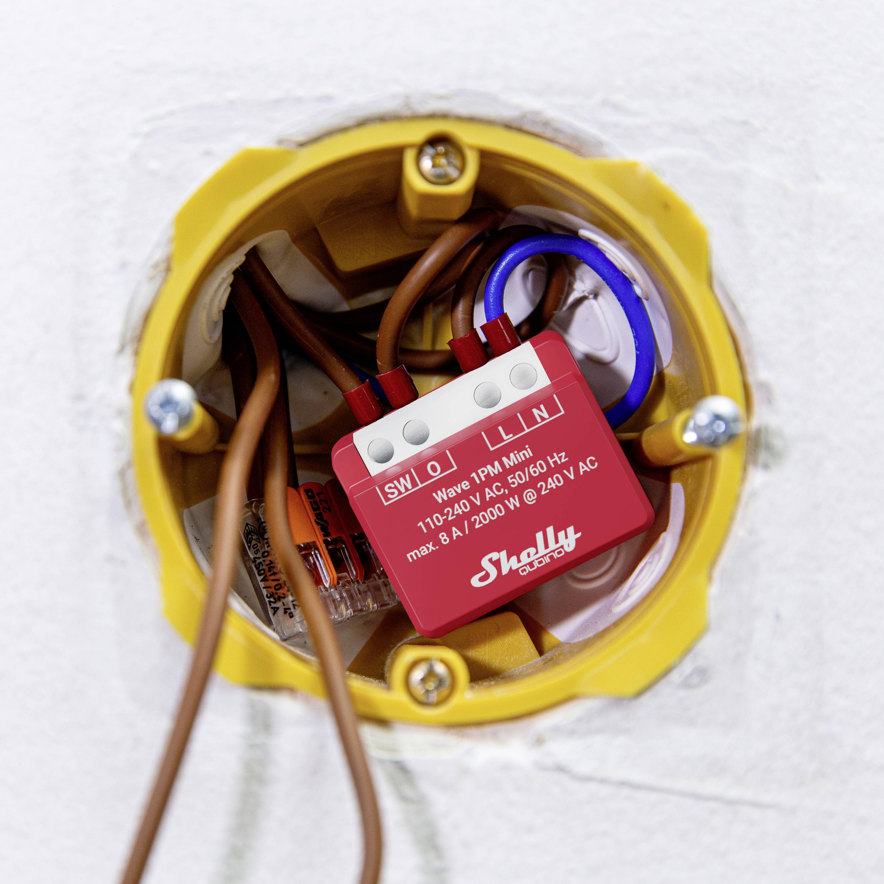Ein rotes Shelly 1PM Smart Relais-Modul in einer Wanddose, umgeben von elektrischen Drähten.