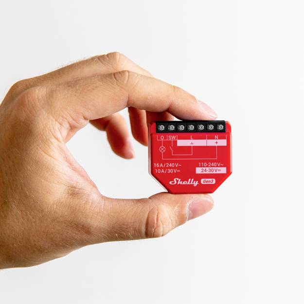 Eine Hand hält ein rotes elektrisches Relaisgerät mit Anschlüssen. Gerät ist für 110-240V, 16A/10A geeignet.