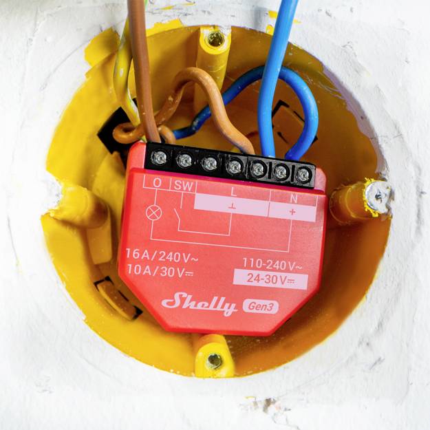 Ein elektrischer Schalter- oder Steuerungsbaustein in einer gelben Wanddose mit mehreren angeschlossenen Drähten in verschiedenen Farben.