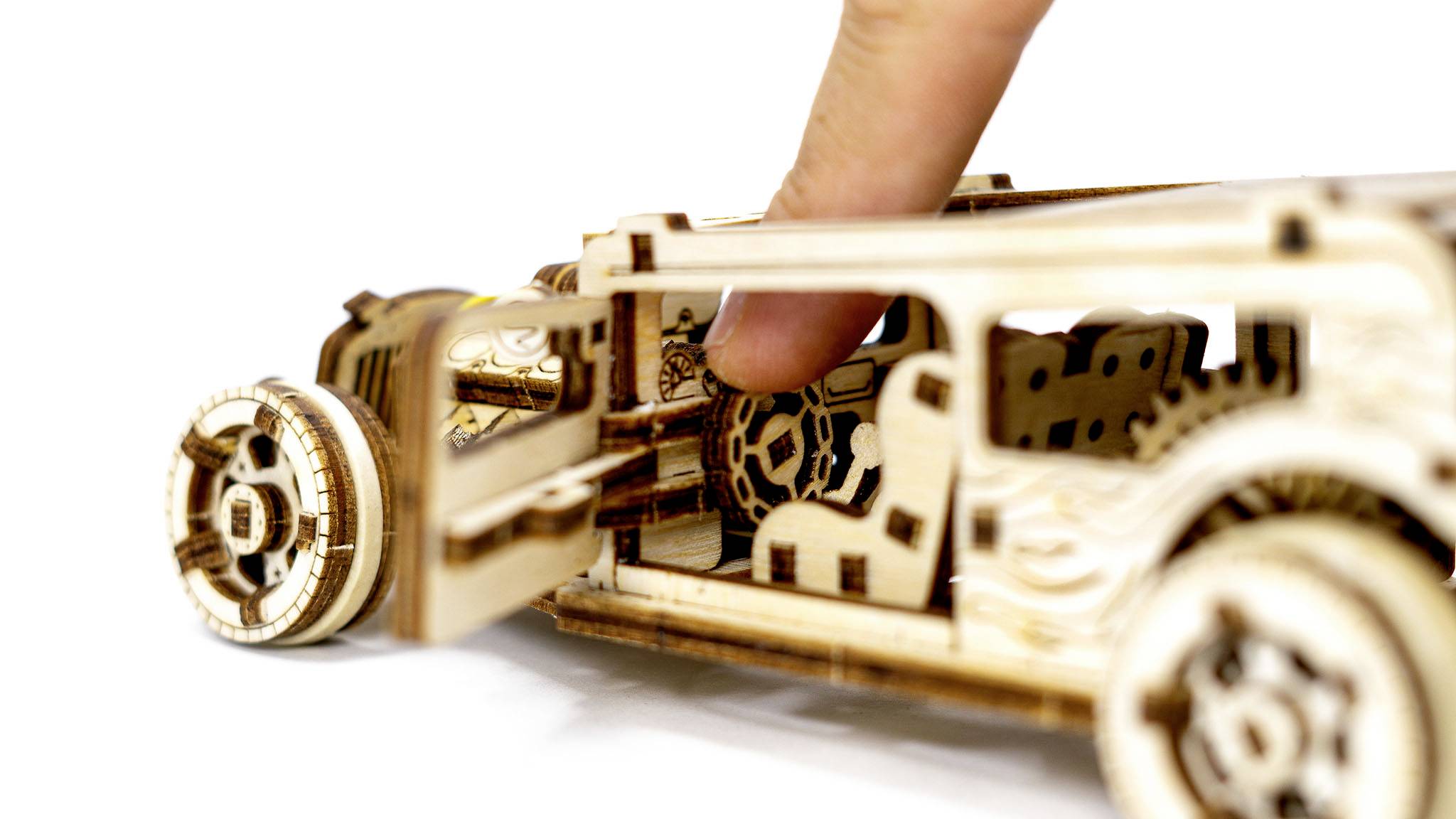 Ein Finger öffnet die Tür eines detaillierten Holzmodellautos mit sichtbarem Innenleben.
