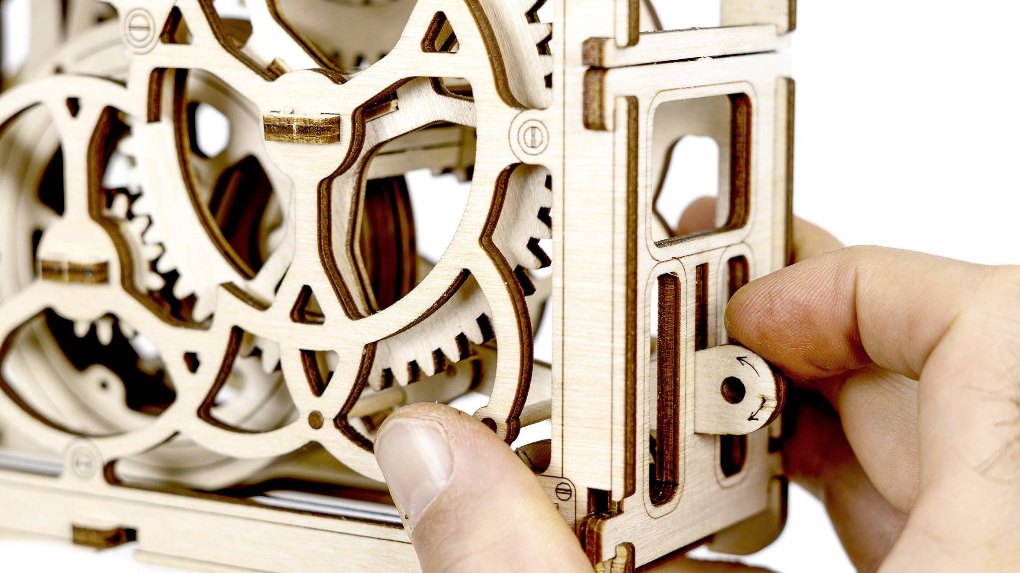 Ein hölzernes Zahnradmodell wird von einer Hand justiert. Die Zahnräder sind kompliziert gestaltet und zeigen mechanische Details.